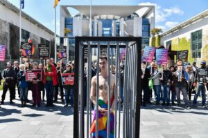 An activist stands naked, wrapped in a rainbow flag, in a mock cage in front of the Chancellery in Berlin on April 30, 2017, during a demonstration calling on Russian President to put an end to the persecution of gay men in Chechnya.